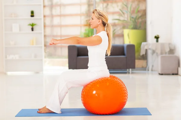 Fit middle aged woman sitting on exercise ball at home