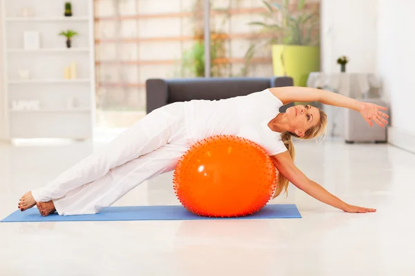 Middle aged woman doing fitness on exercise ball at home