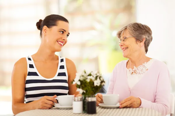 Young woman visiting senior mother and having coffee together