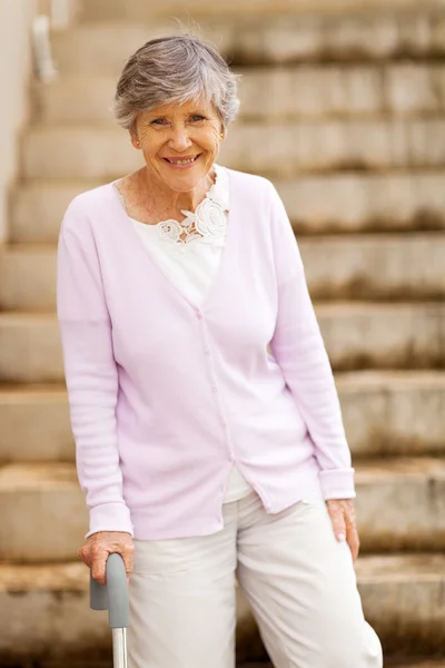 Happy elderly lady standing by stairway with cane