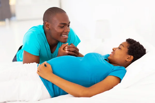 Young african american man talking to pregnant wife on bed