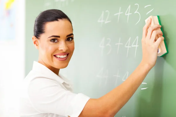 Beautiful female elementary school teacher erasing chalkboard