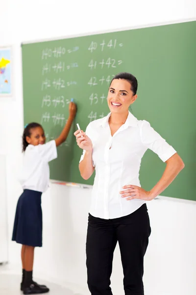 Beautiful primary maths teacher in front of chalkboard in classroom