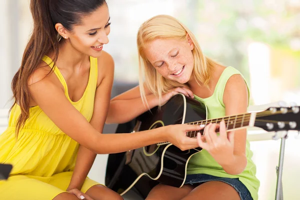 Beautiful music teacher tutoring young girl to play guitar