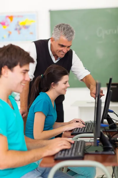 Middle aged teacher helping students with computer