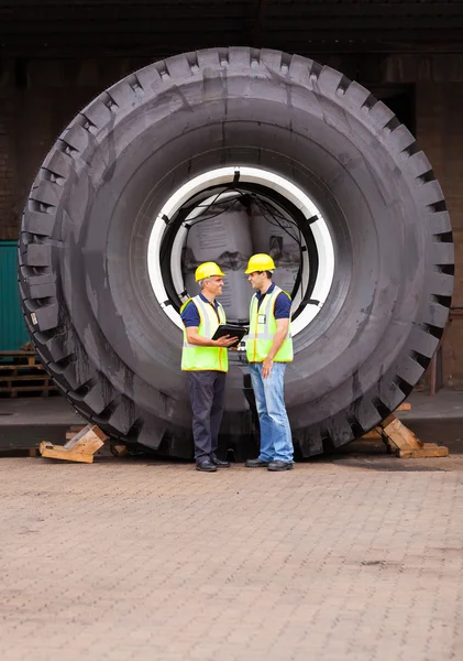 Warehouse workers standing in front of huge tire