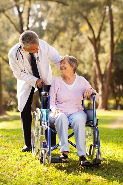 Doctor pushing happy senior patient in wheelchair outdoors
