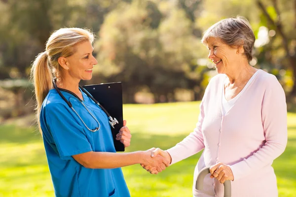 Mid aged nurse handshaking senior patient