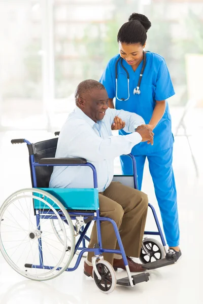 African caregiver helping senior man getting up