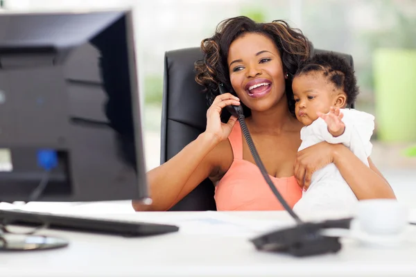African businesswoman talking on landline phone while holding ba