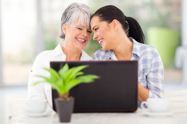 Happy middle aged woman and adult daughter using laptop