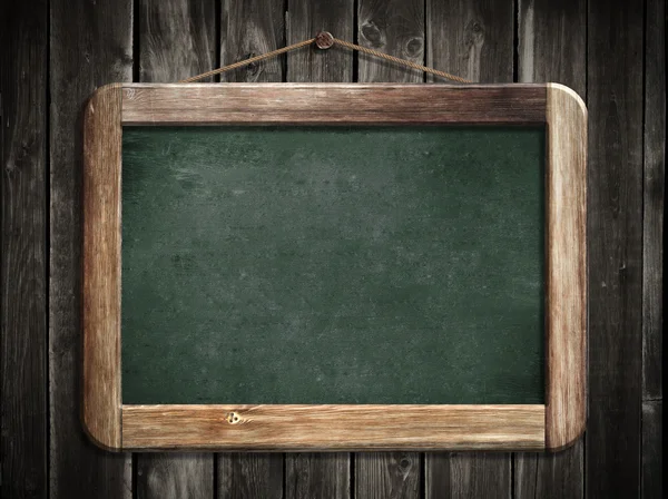 Aged green blackboard hanging on wooden wall as a background for