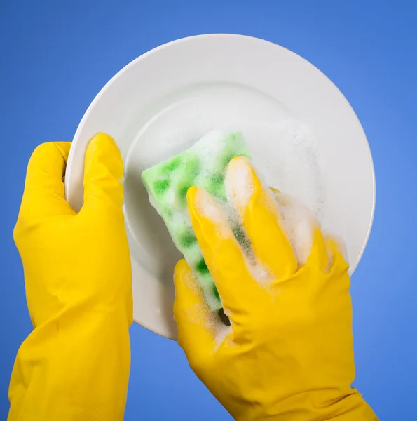 Hands in yellow gloves washing dish on blue background
