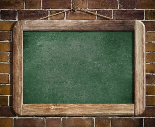 Aged green blackboard hanging on brick wall as a background for