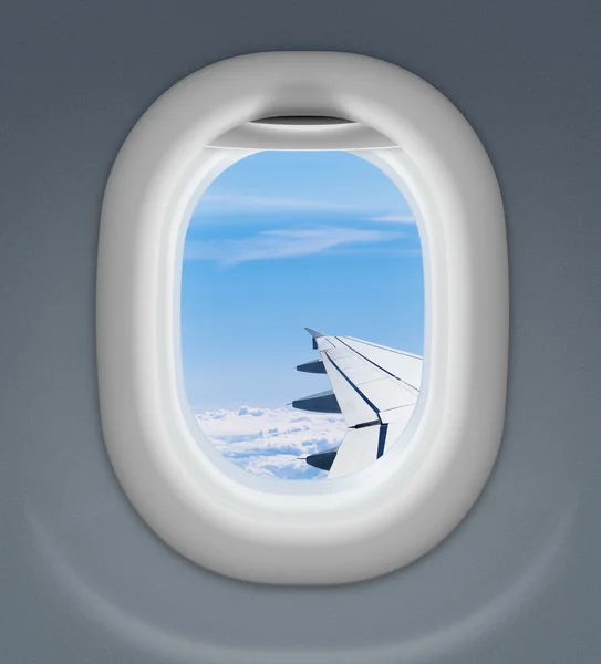 Airplane window with wing and cloudy sky behind