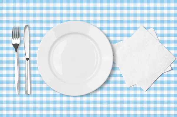 Plate, fork, knife and napkin over blue checked fabric tableclot