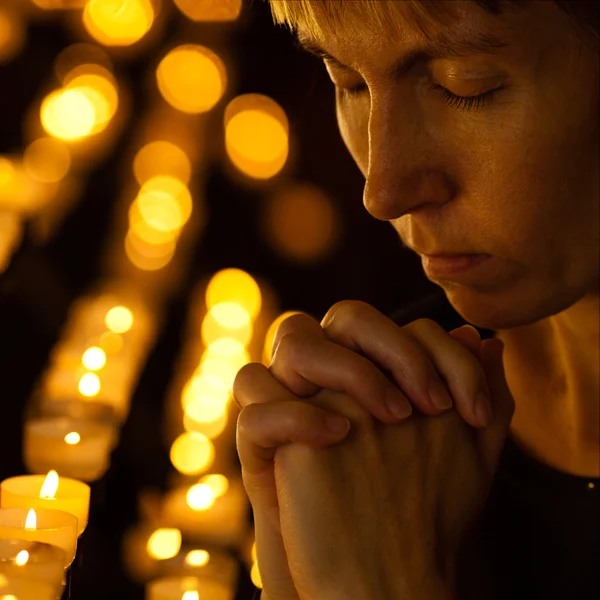 Prayer praying in Catholic church near candles. Religion concept