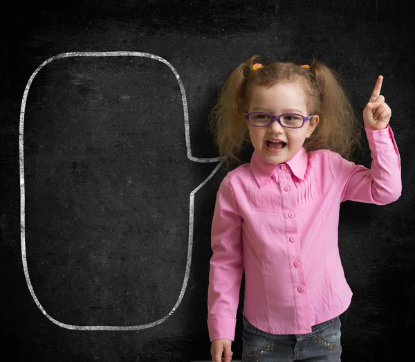 Funny child in eyeglasses standing near school chalkboard as a