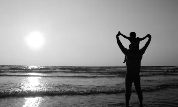 Father and son on a walk by the sea at sunset. Black and white p