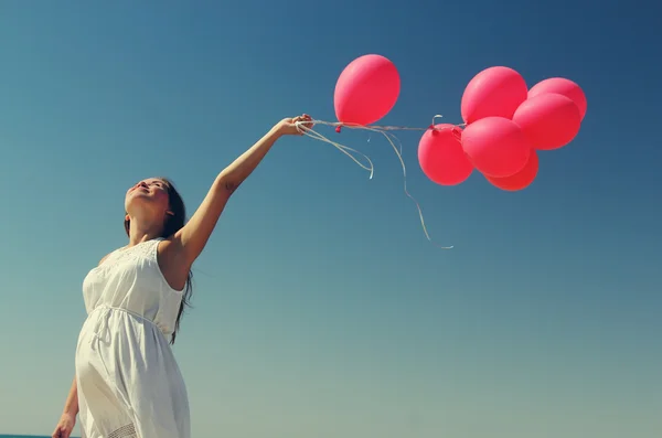 Young pregnant woman holding red balloons