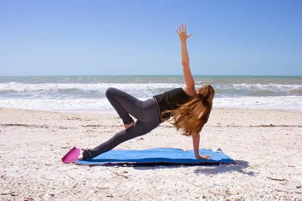 Woman doing yoga exercise on beach in Vasisthasana or side plank