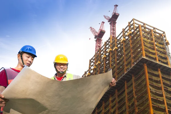 Two construction workers with giant cranes and building