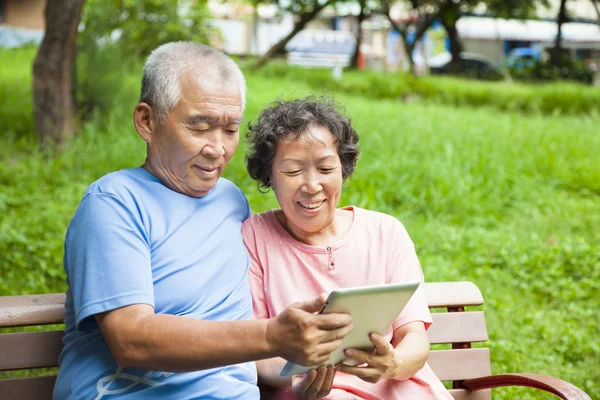 Happy seniors couple with tablet pc in the park