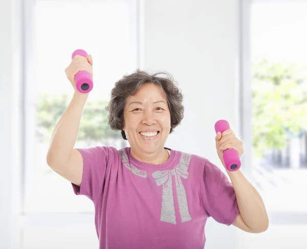 Happy senior woman working out with dumbbells at home