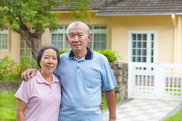 Happy asian senior couple standing in front of a house