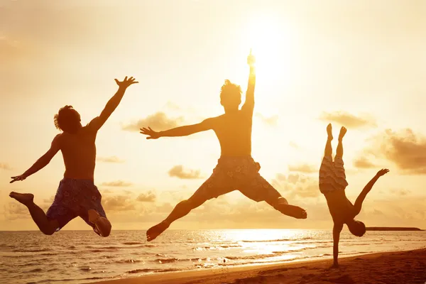 Young people jumping on the beach with sunset background