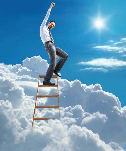 Young confident businessman standing at the ladder high in the sky reaches the top