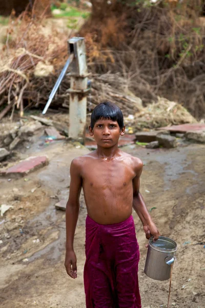Young boy carrying water at the water pump in India