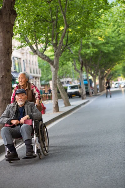 Woman pushing an old man in a wheelchair in the street of Shangh