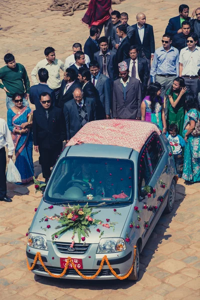 Group of people walking behind the lovers car at a public weddin