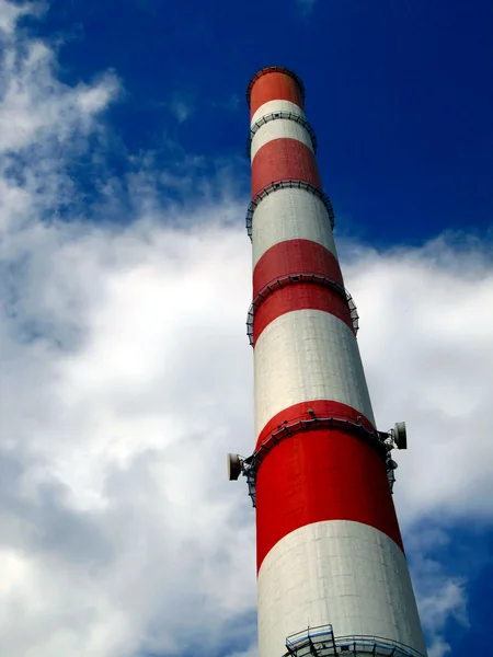 Red and white high chimney in the blue sky with white clouds