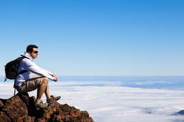 Young Man Having a Rest in a High Peak Over Clouds