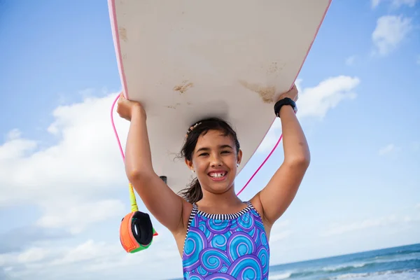 Happy young girl holding surfboard on head