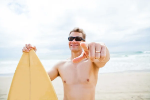 Smiling man with surfboard at beach pointing with finger