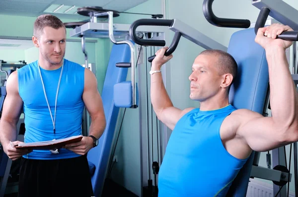 Athlete man in gym with personal fitness trainer