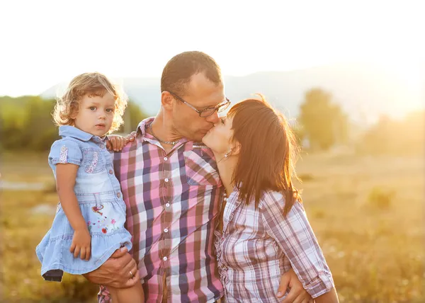 Happy mother, father and daughter in sunset