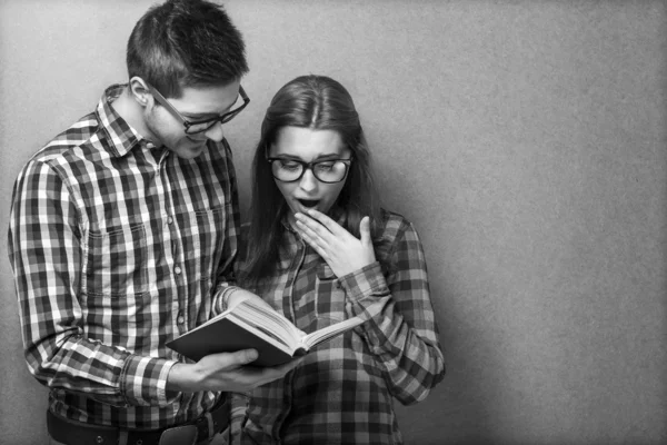 Young couple in clothes and stylish hipster glasses reading a bo