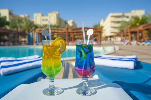 Two cocktail drinks by a tropical pool