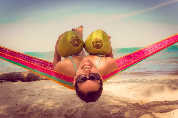 Beautiful young girl lying in a hammock holding two coconuts