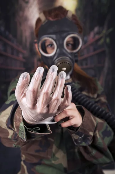 Young girl wearing military uniform and gas mask over dark background