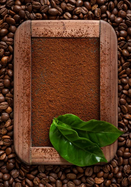 Ground coffee with green leaves on a chalkboard with a background of coffee beans