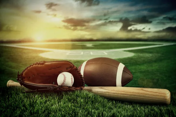 Baseball, bat, and mitt in field at sunset