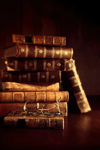 Stack of old books with reading glasses on desk