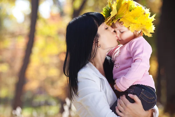 Beautiful young mother kissing her daughter in autumn forest