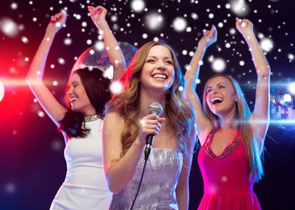 Three smiling women dancing and singing karaoke