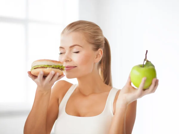 Smiling woman smelling hamburger and holding apple